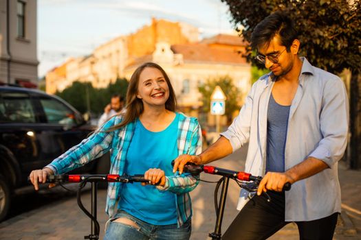 The young couple of diverse people are standing with electric scooters and look at each other