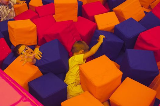 The children are playing with soft cubes in the dry pool. The children of all ages rest in the trampoline park