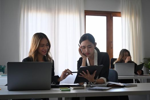 Two female colleagues discussing business project together in office.