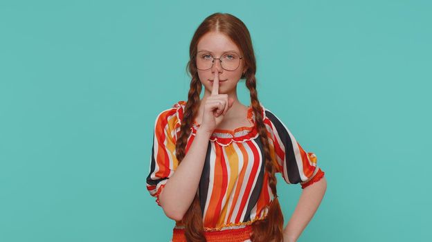 Shh be quiet please. Portrait of redhead girl 20s presses index finger to lips makes silence gesture sign do not tells secret. Young beautiful ginger teenager child isolated on blue studio background
