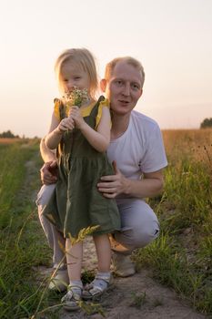 Dad and his blonde daughter are walking and having fun in a chamomile field. The concept of Father's Day, family and nature walks.