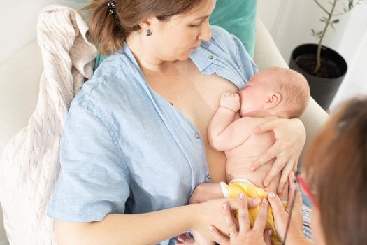 Mom holds her newborn baby in her arms. Mom rests in a chair during comfort breastfeeding