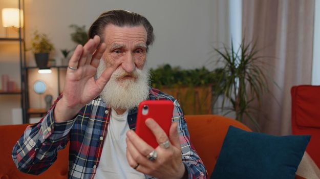 Senior old grandfather man wearing earphones making phone online conversation call with family sitting at home living room couch. Elderly retired grandpa pensioner enjoying mobile loudspeaker talking