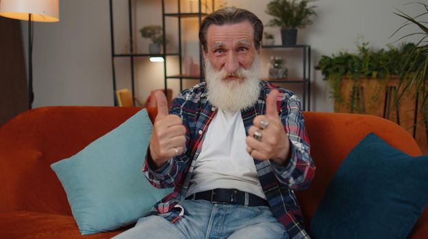 Like. Happy senior old grandfather man looking approvingly at camera showing thumbs up, like sign positive something good, positive feedback sits at home room couch. Elderly retired grandpa pensioner