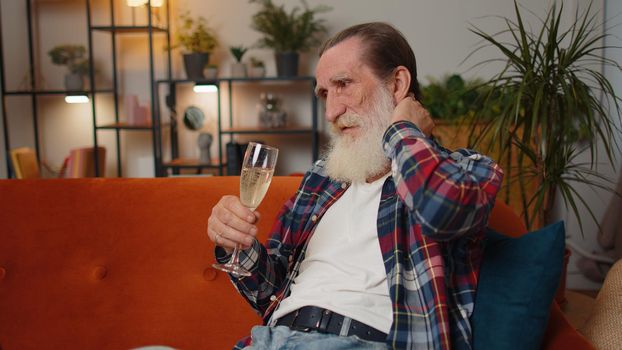 Sad senior old grandfather man sitting at home looks pensive suffers from unfair situation, illnesses, despair drinking champagne. Problem, break up, depressed feeling bad annoyed, burnout, bankruptcy