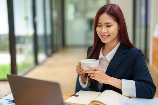 Asian female worker using computer and budget documents on desk.