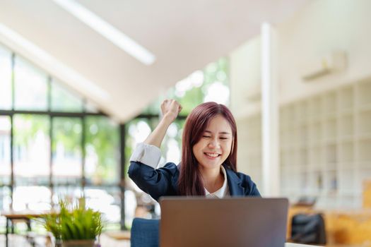 cheerful Asian celebrating her victory online with her laptop.