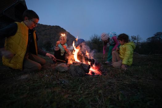 Children after hiking have a picnic - group of happy friends frying sausages on campfire