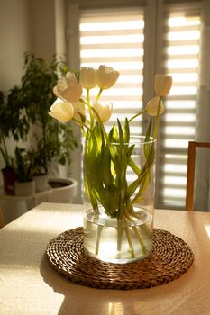 Spring flowers - white tulips in glass vase on wooden table. Natural light at the elegant scandi kitchen interior.
