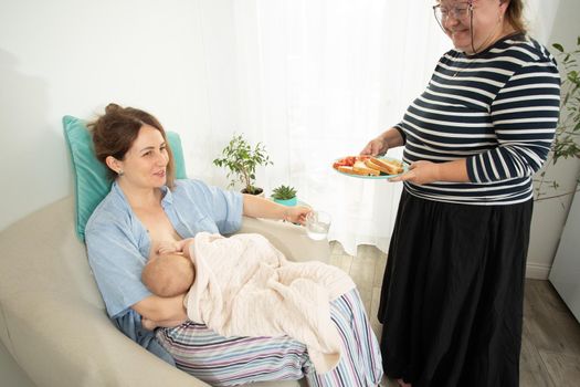 Elder woman helps to eat for new mother when she breastfeeds her baby. Motherhood support