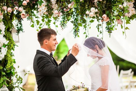 Wedding couple under the flower arch at the wedding ceremony outdoors in the park