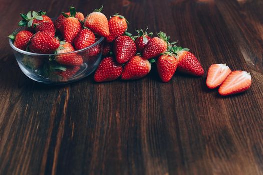 Fresh and juicy strawberries in a glass bowl on wooden background in rustic style, healthy sweet food, vitamins and fruity concept. Copy space for text