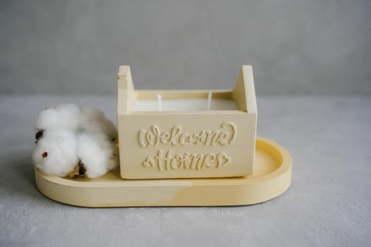 An interior item. Soy candle in a yellow plaster candlestick. Scented candle on a stand. A candlestick in the shape of a house. The inscription on the candlestick Welcome home. Lettering.