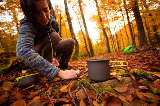 Woman uses portable gas heater and pan for cooking outdoors while camping. Collapsible bottles to save space in your backpack.