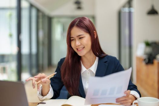 Asian female worker using computer and budget documents on desk.