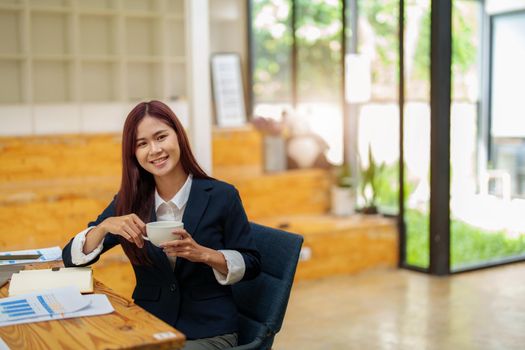 Asian female worker using computer and budget documents on desk.