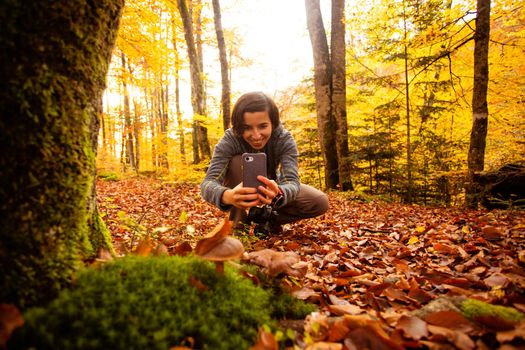 Woman in the forest takes pictures of a mushroom usinag smartphone. Nature park walk, photography as a hobby.