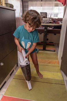 A sweet little boy vacuums the caravan while on vacation. A cute boy is cleaning the caravan