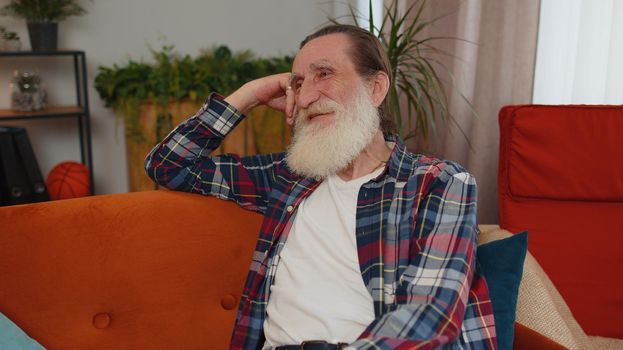 Portrait of happy calm senior old grandfather man pensioner smiling friendly, glad expression looking away dreaming resting, relaxation feel satisfied concept good news sitting on sofa at home room