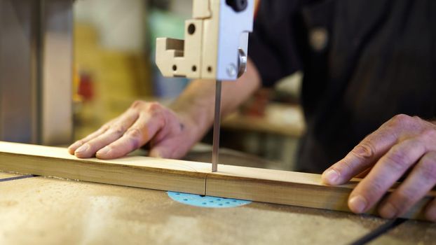 Handwork, carpentry concept, woodworking. Carpenter working in in factory atelier. Joiner labourer cuts wooden plank on jigsaw machine. High quality photo