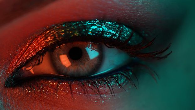 Extreme close up of human eye iris under violet neon light. Female with beautiful makeup, glitter shadows. Woman green eye. Beauty, cosmetics, night club lifestyle concept. High quality photo