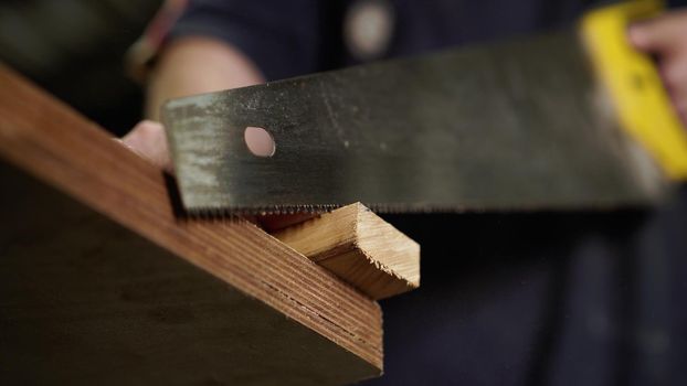 Handwork concept, woodworking workshop. Carpenter saws wooden board with hand jigsaw. Close-up view. . High quality photo