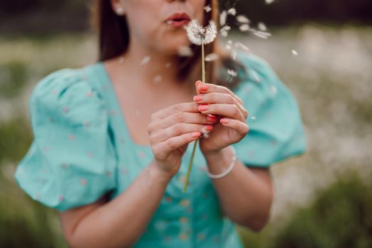 Happy woman beautiful blowing on dandelion in park. Girl in vintage blue dress. Wishing, joy concept. Springtime, aesthetic portrait. High quality photo