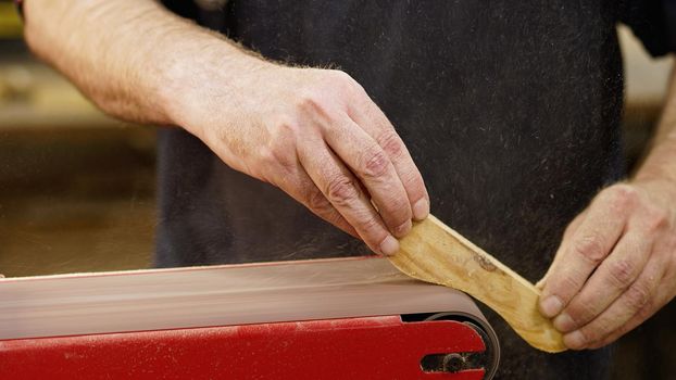 Hands of carpenter sharpens wooden part on grinding machine. Handwork concept, woodworking workshop. High quality photo