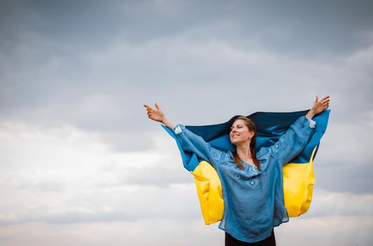Smiling ukrainian woman with national flag on sky background. Portrait of young lady in blue embroidery vyshyvanka.Ukraine, independence,freedom, patriot symbol, victory in war.High quality