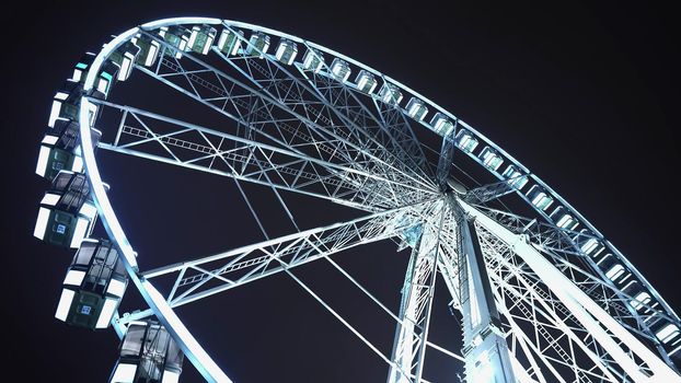 Brightly lit ferris wheel ride, which spinning at night or evening carnival. Low angle. Colored lights flashing. Concept of amusement park, fair, thrill. High quality photo