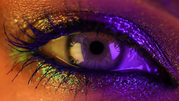 Close-up of woman eye under neon light. Female with beautiful makeup, glitter shadows. Beauty, cosmetics, night club lifestyle concept. High quality photo