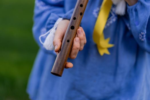 Woman playing woodwind wooden flute - ukrainian sopilka outdoors. Folk music, culture concept. Musical instrument. Lady in traditional embroidered shirt - blue vyshyvanka. High quality photo