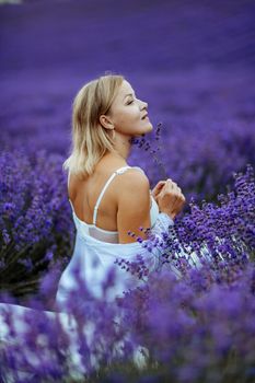 A middle-aged woman sits in a lavender field and enjoys aromatherapy. Aromatherapy concept, lavender oil, photo session in lavender.