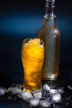 Beer cocktail in a beer glass on a black background with pieces of ice next to a beer bottle with no inscriptions. A refreshing summer cocktail. Beer Slushie Cocktail