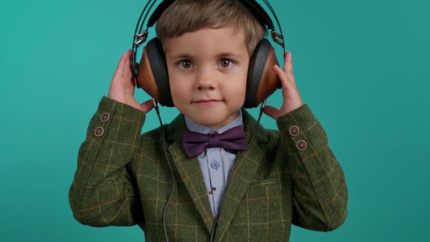 Handsome little toddler boy listening to music with old headphones, child having fun, funny dancing in studio on blue background. Dance, radio, analog concept. High quality photo