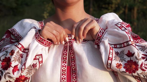 Ukrainian woman fastens button on embroidered shirt with traditional ornament. National costume - vyshyvanka, texture, design, folk, handmade craft needlework. High quality photo