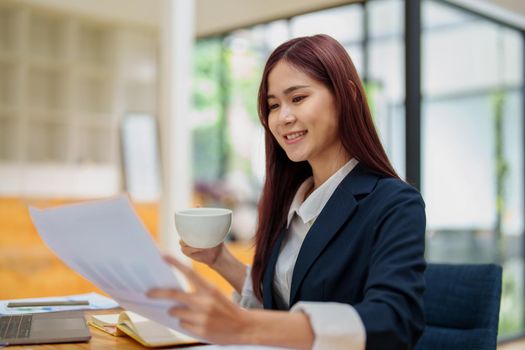 Asian female worker using computer and budget documents on desk.