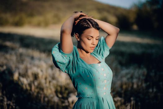 Portrait of young rural elegant woman posing on nature background. Sexy languid lady touching hair, enjoying summertime, sun rays. Vintage styled dress. High quality photo
