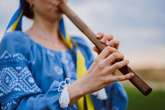 Woman playing woodwind wooden flute - ukrainian sopilka outdoors. Folk music, culture concept. Musical instrument. Lady in traditional embroidered shirt - blue vyshyvanka. High quality photo