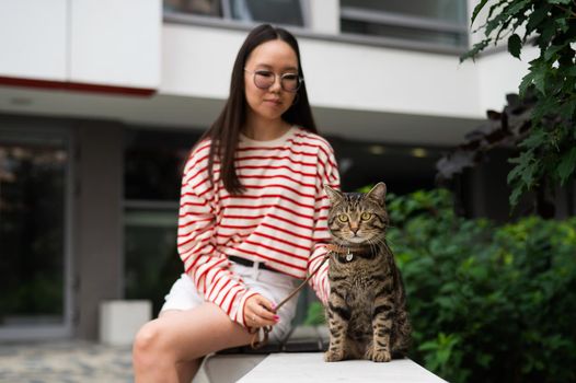 Young woman and tabby cat sitting on a bench outdoors