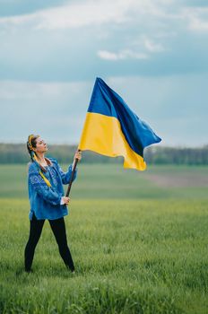 Beautiful ukrainian woman with national flag on green field background. Young lady in blue embroidery vyshyvanka. Ukraine, independence, freedom, patriot symbol, victory in war. High quality photo