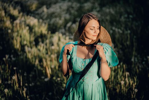 Young stylish woman in vintage dress and straw hat alone on nature in countryside. Carefree lifestyle, romantic girl. Retro fashionista like from novel. High quality photo
