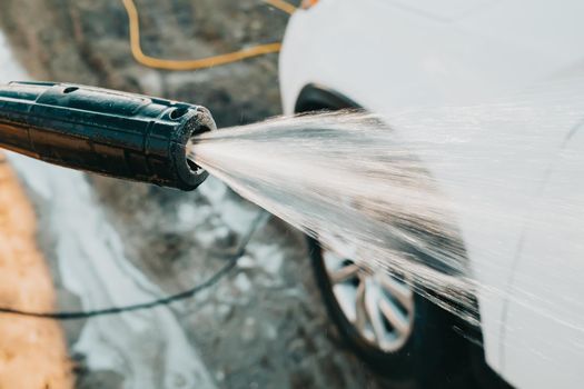 Manual car wash with jet of high pressure water. Worker washes white automobile outside on territory of private house. Caring for vehicle concept. High quality photo