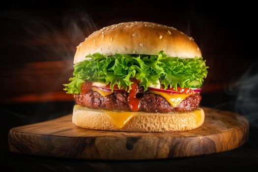 Tasty burger with smoke, fast food concept. Fresh homemade grilled hamburger with meat patty, tomatoes, cucumber, lettuce, onion and sesame seeds. Unhealthy lifestyle. Food background. . High photo