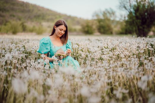 Gorgeous woman reading old paper book. Lady in retro or vintage dress reading interesting novel while sitting on nature among fluffy dandelions. Aesthetic scene, pastel natural colors. quality photo