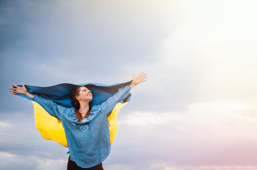 Happy free ukrainian woman with national flag on dramatic sky background. Portrait of lady in blue embroidery vyshyvanka shirt. Copy space. Ukraine, independence, patriot symbol. High quality photo