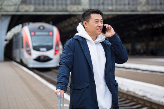 Business man Asian man at the train station having fun talking on the phone, a passenger arrived on a business visit to a new city, with a large suitcase of luggage