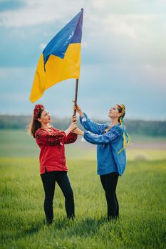 Happy ukrainian women raised national flag, it flies as symbol of love for Motherland. Friends in embroidery vyshyvanka - national blouses. Ukraine, independence, patriot symbol. High quality photo