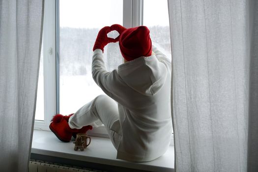 A woman in a white suit sits on the windowsill and looks out the winter window. High quality photo