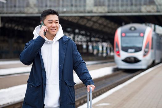 Business man Asian man at the train station having fun talking on the phone, a passenger arrived on a business visit to a new city, with a large suitcase of luggage